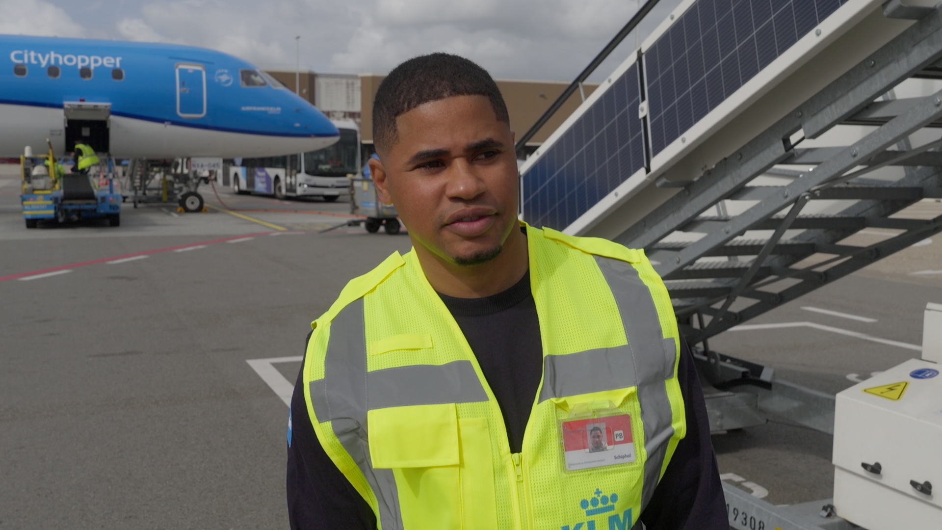 Een KLM-medewerker in een geel veiligheidshesje op het platform, met achter hem een toestel van KLM Cityhopper en een vliegtuigtrap
