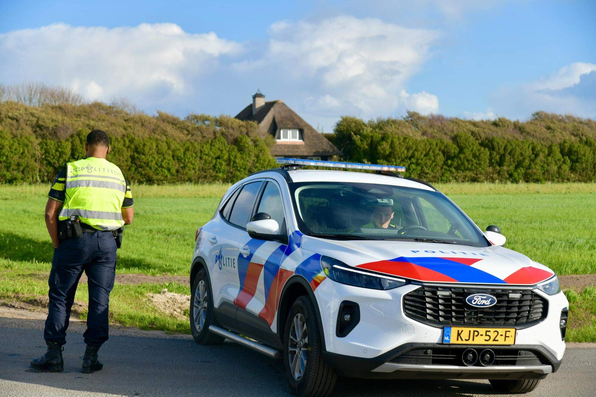 Een politieauto en een agent in geel hesje op een smalle polderweg bij Callantsoog, met weilanden en duinen op de achtergrond