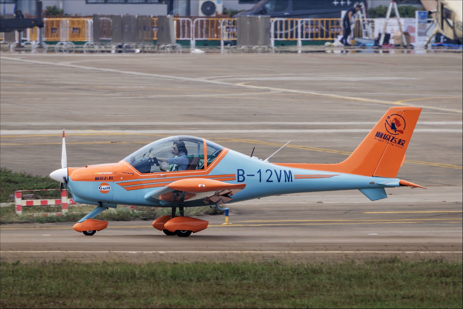 Een blauw-oranje tweezits laagdekker met glazen kap en de registratie B-12VM taxiet over een platform